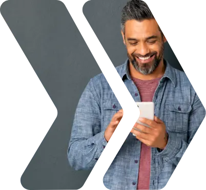 A person leaning against a wall and smiling while interacting with his phone